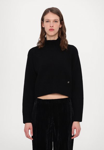 Schwarzer, kurzer Pullover mit geripptem Kragen und Bündchen. Weicher Strickstoff. Kombiniert mit schwarzen, plissierten Hosen, die einen monochromen Look schaffen.