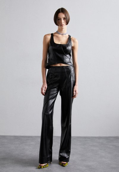 Fekete bőrből készült, cropped fazonú felső, magas nyakkal, fekete bőrből készült, testhez simuló nadrággal párosítva. Sárga részletekkel ellátott pántos magassarkúk egészítik ki a szettet.