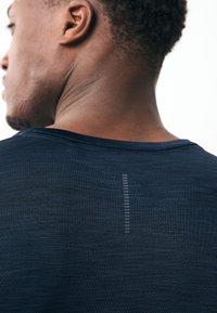 Marineblaues Sportshirt mit kurzen Ärmeln, figurbetontem Design und glatter Textur. Auf der Rückseite befindet sich ein vertikales reflektierendes Detail.