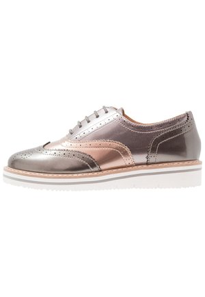 Oxformsko i metallisk rosaguld og sølv med brogue-perforeringer og tyk hvid platformsål, set fra siden.
