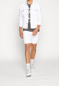 Chaqueta de mezclilla blanca sobre una camiseta gráfica gris, combinada con pantalones cortos blancos y zapatillas ligeras. Textura suave, ajuste casual y diseño minimalista.
