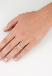 Silberner Bandring mit schlankem Design, der eine gerade Reihe kleiner, klarer Steine aufweist. Hand auf einem hellen, neutralen Hintergrund platziert.