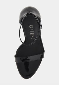 Černé lakované kožené sandály na vysokém podpatku se zavřenou špičkou, kotníkovým páskem a mírným prohnutím podrážky. Vyznačují se hladkým, lesklým povrchem s minimálními detaily.
