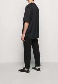 Černé síťované tričko s krátkým rukávem a volným střihem, spárované s černými zúženými kalhotami a černými teniskami. Texturovaná tkanina s otevřenou vazbou.