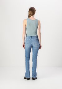 Light blue flared jeans with a fitted shape and mid-rise waist, paired with a sleeveless, ribbed light blue top, viewed from the back.