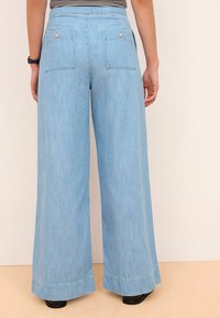 Jean large bleu clair avec une texture lisse, doté de deux poches arrière et de détails à boutons, ourlé avec une finition droite.