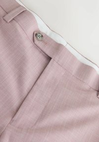 Ceinture de pantalon rose clair texturée avec une doublure intérieure blanche et un seul bouton gris fixé sur le côté.