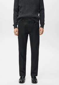 Pantalones de mezclilla oscura, diseño de pierna recta, con trabillas para cinturón y bolsillos delanteros, combinados con un suéter gris texturizado y zapatos negros.