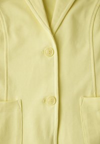 Gul blazer med en mjuk textur, försett med två knappar, en slagkrage och två framfickor för en strukturerad siluett.