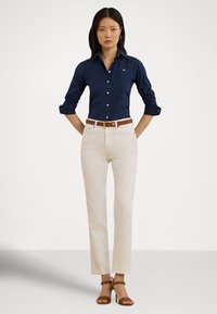 Modra mornarska srajca s srajčnimi gumbi in zavihanim rokavom, bež hlače s pravo nogo, rjav pas in rjavi sandali s trakovi. Gladek tekstil z utečeno prileganjem.