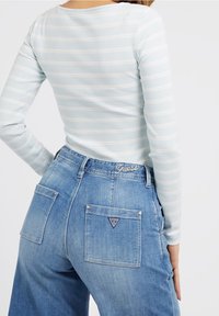 Ljust blå ribbad långärmad topp med vita ränder, kombinerad med högmidjade blå denimjeans som har två bakfickor och en logodetalj.