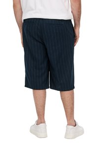 Shorts bleu marine à rayures, fabriqués en tissu léger, offrant une coupe décontractée, un design jusqu'aux genoux et deux poches arrière, associés à des baskets blanches.