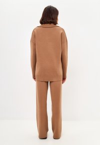 Pulover casual din tricot maro, cu guler înalt, croială supradimensionată și accente cu model ondulat, asortat cu pantaloni largi. Textură netedă.