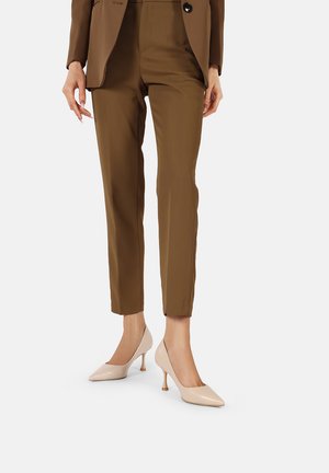 Pantaloni marroni su misura abbinati a tacchi in vernice beige. I tacchi presentano una silhouette affusolata e un design di tacco curvo distintivo.