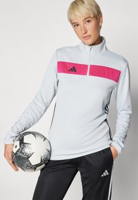 Light blue athletic top with a pink and black horizontal stripe, zip collar, paired with black pants and a patterned soccer ball.