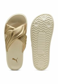 Guldiga slidesandaler med korsremdesign i slätt material. Texturerad vit sula med greppmönster. Puma-logotyp på innersulan.