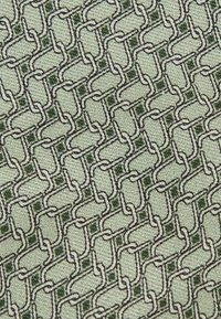 Textiel met een geometrisch kettingpatroon in donkergrijs en groen op een lichtgroene achtergrond, met een gestructureerd oppervlak.