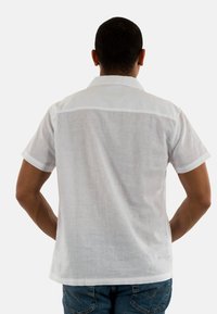 Camisa blanca de manga corta hecha de una tela ligera, que presenta un cuello simple y un color sólido con una textura sutil, combinada con jeans azules.