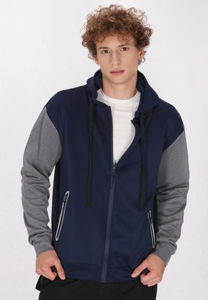 Marineblaue und graue Zip-Jacke mit Kapuze, seitlichen Taschen und einem glatten, leichten Stoff mit einem kontrastierenden Design.