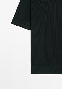 Mörkgrön ribbad topp med korta ärmar och rundad nederkant. Har en texturerad tyg och en figurnära design vid ärmsluten och nederkanten.