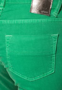 Jeans de mezclilla verdes con un bolsillo trasero con un borde cosido. Una etiqueta plateada brillante con "JOOP!" está sujeta a la cinturilla.