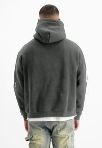 Grijze sweatshirt met capuchon, met een relaxte pasvorm, zachte stof en gedetailleerde stiknaad. Gedragen over lichtgekleurde broeken.