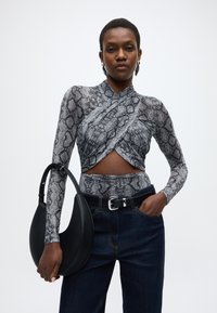 Haut imprimé peau de serpent avec un design croisé, manches longues et découpe au niveau de la taille, associé à un jean noir taille haute et un sac à main croissant.