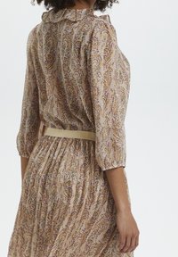 Långärmad, mönstrad klänning i lätt tyg med en volangkrage och elastiska ärmslut, åtdragen i midjan med ett beige bälte.