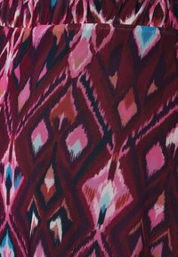 Närbild av tyg med geometriska diammmönster i nyanser av rosa, vinröd, blått och vitt på en samlad sektion.