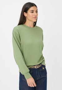 Felpa verde chiaro a maniche lunghe con scollatura rotonda e maniche con polsini, abbinata a jeans blu scuro e una cintura con stampa leopardata.