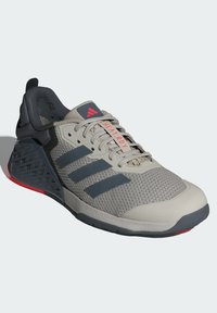 Szare buty sportowe z siateczkową cholewką, z trzema ciemnymi paskami, wyściełanym kołnierzem i wzorzystym gumowym obcasem z czerwonymi akcentami.