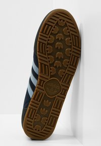 Adidas-sneakersula med en beige gummiyttersula med ett mönster av räfflor och logotyp, mörkblå ovandel med ljusblå ränder.