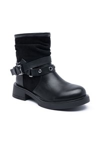 Bottines noires avec un petit talon, tige en daim repliée et bandoulières en cuir décoratives avec boucle en métal et clous.