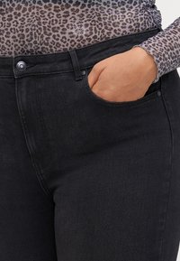 Black denim jeans feature a classic five-pocket design with a visible side pocket, subtle stitching, and a close-fitting silhouette.