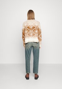 Suéter de punto con un patrón abstracto en marrón y crema, con un cuello redondeado y un ajuste holgado, combinado con jeans rectos de un azul claro.