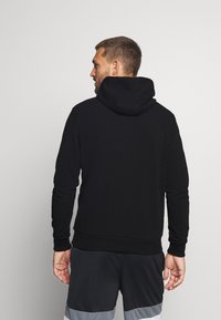 Felpa nera con cappuccio, caratterizzata da una vestibilità regolare, polsini e orlo a coste. Il modello la indossa con pantaloni corti scuri.