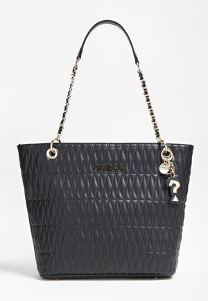 Czarna pikowana torba na ramię z łańcuszkiem i skórzanym paskiem, złote logo GUESS oraz zwisające charmsy, w tym znak zapytania i okrągła zawieszka.