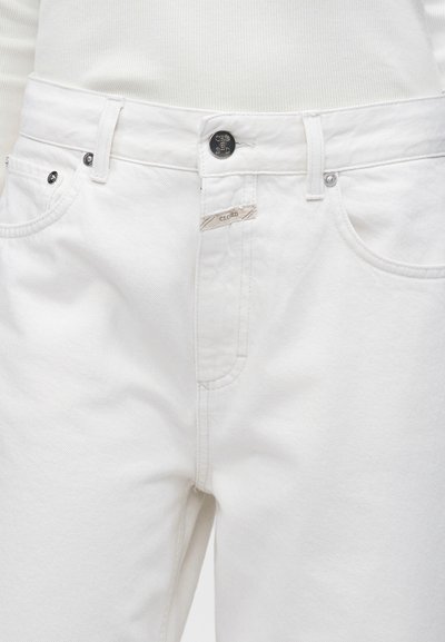 Personne portant un jean blanc taille haute et un haut blanc côtelé, montrant la ceinture avant, le bouton, les passants de ceinture et les poches.