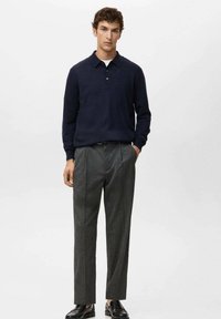 Granatowy dzianinowy polo z kołnierzykiem, na trzy guziki, w połączeniu z jasnoszarymi, dopasowanymi spodniami i czarnymi skórzanymi butami. Gładka faktura, swobodny krój.