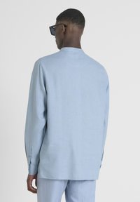 Camicia azzurro chiaro con maniche lunghe, taglio dritto, polsini con bottone e colletto rotondo. Il tessuto ha una texture liscia e pulita.