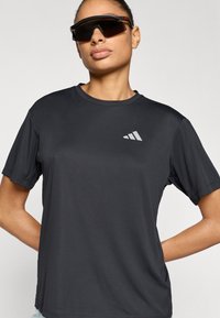 Μαύρο αθλητικό t-shirt με στρογγυλή λαιμόκοψη και κοντά μανίκια, φτιαγμένο από απαλό, διαπνέον ύφασμα· περιλαμβάνει ένα μικρό λευκό λογότυπο στο στήθος.