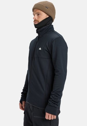 Black zip-up jacket features a textured fabric, subtle seams, and a small logo on the chest; paired with a brown knit beanie.