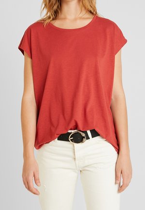 Punainen lyhythihainen paita, jossa on pyöreä kaula-aukko, soljuva muotoilu ja pehmeä rakenne, yhdistettynä valkoisiin kuluneisiin farkkuihin ja mustaan vyöhön.