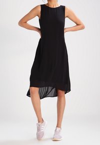 Černé bezrukávové šaty s křivkovým lemem, které mají vzdušnou strukturu. Nosené s světle růžovými teniskami, což podtrhuje neformální vzhled.