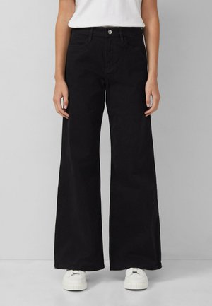 Zwarte wijdemontje jeans van katoen, met een hoge taille, voorzakken en een enkele knoopsluiting. Gecombineerd met witte sneakers.