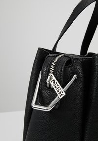 Mustan nahkalaukun, jossa on teksturoitu pinta, hopeanvärinen vetoketju ja metalliosat, joissa on logokoriste. Pyöreät yläkahvat.