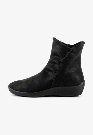 Bottine en suédine noire avec un bout rond et une semelle en wedge texturée et basse. Elle présente une fermeture éclair sur le côté et des détails de couture subtils.