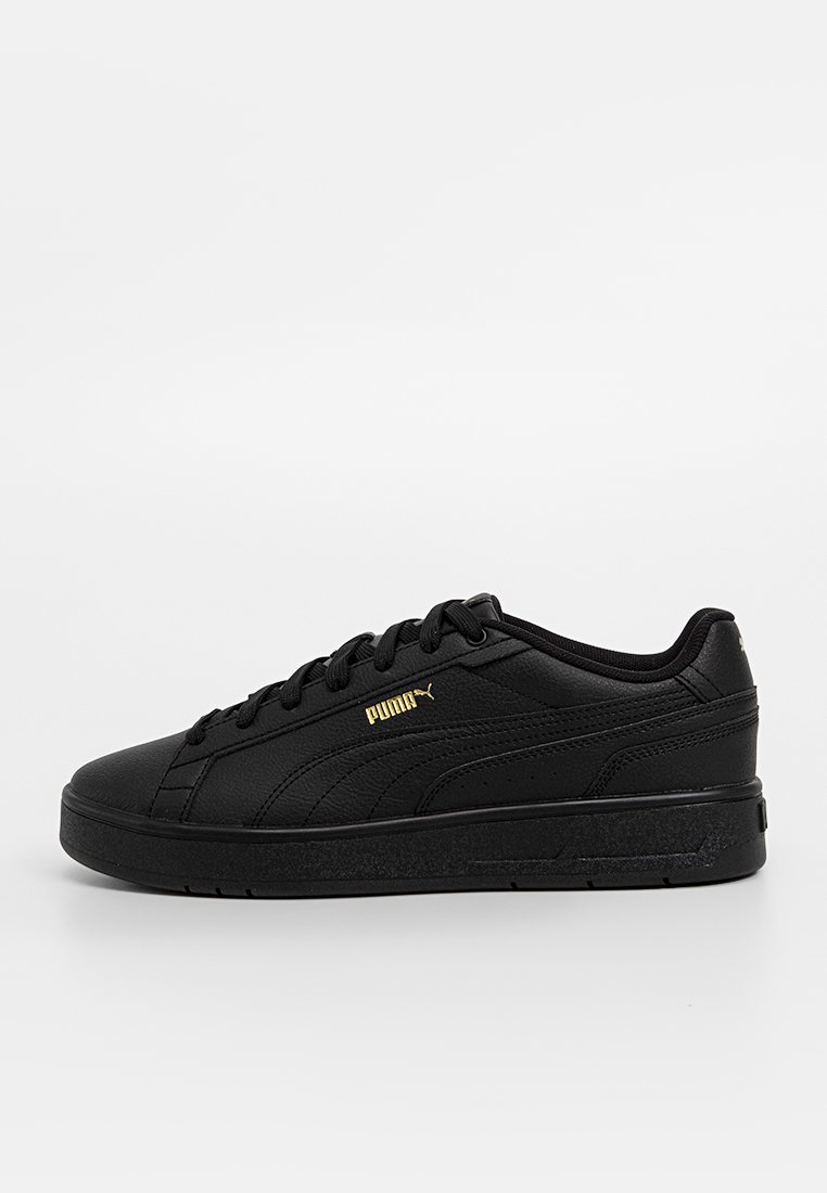 Baskets de sport noires en matériau synthétique lisse, avec un design à tige basse, des accents de logo dorés et une semelle en caoutchouc texturée.