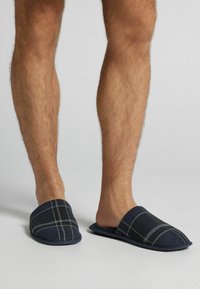 Granatowe kapcie w kratkę z miękką górą z materiału i wyściełaną podeszwą. Posiadają wygodny fason wsuwany oraz szary wzór w kratkę dla dodatkowego akcentu.