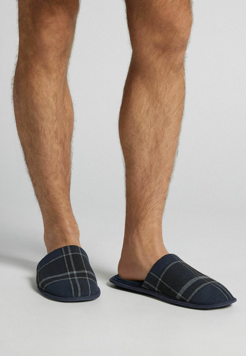 Granatowe kapcie w kratkę z miękką górą z materiału i wyściełaną podeszwą. Posiadają wygodny fason wsuwany oraz szary wzór w kratkę dla dodatkowego akcentu.